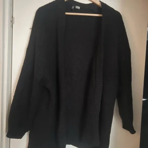 Svart stickad kofta - Säljer en svart stickad kofta med långärmad design. Perfekt för kyligare dagar och enkel att matcha med olika outfits. Koftan har en öppen front och är gjord i ett mjukt material för extra komfort.