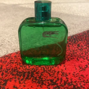 Grön parfymflaska från Lacoste - Säljer en grön parfymflaska från Lacoste med den ikoniska krokodilloggan. Flaskan har en fyrkantig form och rymmer 100 ml. Perfekt för den som gillar en fräsch och sportig doft. Flaskan är stilren och enkel att ta med sig.