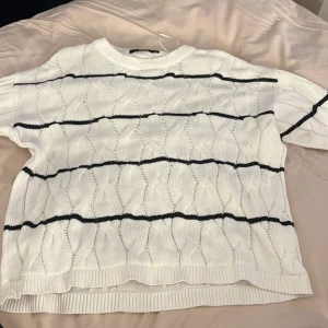 Vit stickad tröja från BikBok - Säljer en vit stickad tröja från BikBok med svarta ränder. Tröjan har en avslappnad passform och långa ärmar, perfekt för kyligare dagar. Den är mjuk och bekväm att bära. Passar bra till jeans eller kjol för en stilren look.