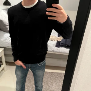 Svart tröja från Uniqlo - Säljer en stilren svart tröja från Uniqlo i storlek M men sitter som en S!Tröjan har en klassisk design med långa ärmar och rund hals. Perfekt för en enkel och snygg look. Stickad!