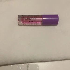 Cherry Lip Oil - Cherry Lip Oil i en genomskinlig tub med lila lock. Perfekt för att ge läpparna en glansig finish och extra fukt. Den har en lätt rosa ton och doftar härligt av körsbär. Den är ny och oöppnad 🤟✌️✌️✌️