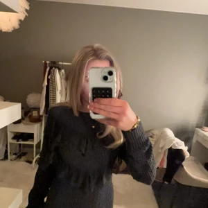 stickad tröja med volang detaljer  - Säljer en snygg mörkblå stickad tröja med volangdetaljer framtill. Tröjan har långa ärmar och en ribbad kant vid ärmslut och nederkant. Perfekt för kyligare dagar!