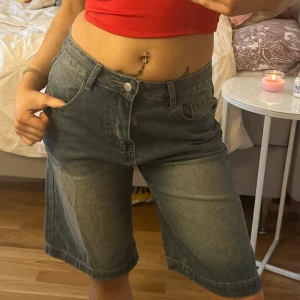 Jeansshorts i knälång modell - Säljer ett par klassiska jeansshorts i knälång modell. De är blå och har en normal passform med femficksdesign och knappgylf. Perfekta för en avslappnad stil.