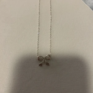 Silverhalsband med rosett - Elegant silverhalsband med en liten rosett som hänge. Perfekt för att ge en subtil och stilren touch till din outfit. Kedjan är tunn och smidig, vilket gör den bekväm att bära hela dagen.