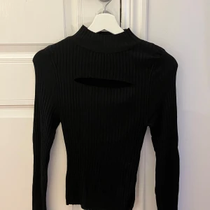 Svart ribbad topp från Gina Tricot - Snygg svart ribbad topp från Gina Tricot med lång ärm och en unik öppen detalj ovanför bröstet. Perfekt för en stilren look.