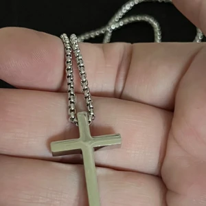 Silverfärgat korshalsband - Stilrent silverfärgat halsband med ett enkelt korshänge. Kedjan är av kulmodell och ger en modern touch till det klassiska korset. Perfekt för både vardag och speciella tillfällen.