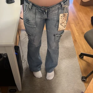 Blå jeans (cargopants) med fickdetaljer - Snygga blå jeans/cargopants med flera fickor och coola detaljer. Lågmidjade och utsvängda. Väldigt unika och skitsnygga. I nyskick! Har en jättefin passform och passa perfekt i längden på någon som är 168cm lång.❤️