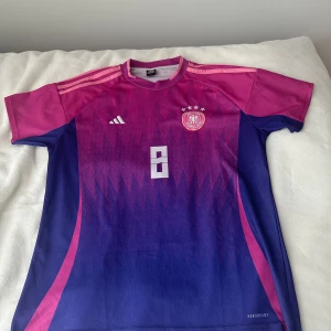 Fotbollströja med nummer 8 - Snygg fotbollströja från Adidas i rosa och blått med nummer 8 på framsidan och baksidan. Tröjan har korta ärmar och ett coolt mönster. Perfekt för fotbollsfans!