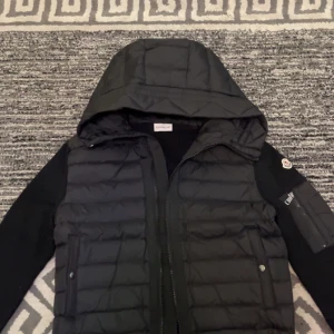 Moncler cardigan - Snygg svart jacka från Moncler med quiltad design och huva. Jackan har dragkedja framtill och ribbade ärmar. Perfekt för kyligare dagar och ger en stilren look.