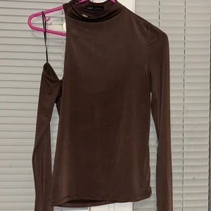 Brun oneshoulder topp - Snygg brun oneshoulder topp från Pull & bear. Toppen har en unik design med en lång ärm och en öppen axel. Perfekt för att ge en trendig touch till din outfit.