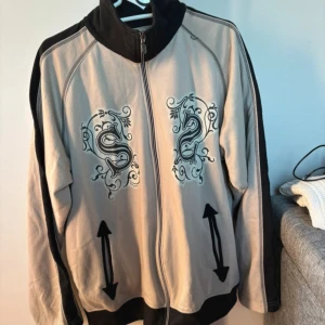 Beige och svart jacka med tryck - Beige och svart tröja med dragkedja och tryck på framsidan och text 'university' på baksidan. Den är köpt second hand! Jätte snygg men använder inte längre. Kan mötas upp i sthlm (skriv priv isf)