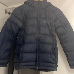 Mörkblå dunjacka från Peak Performance - Säljer en mörkblå dunjacka från Peak Performance. Jackan har en dragkedja framtill och är långärmad med en stilren design. Perfekt för kalla dagar med sin varma och bekväma passform.