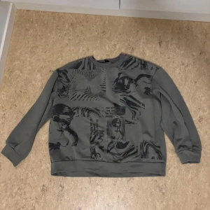 Grå sweatshirt med abstrakt mönster - Säljer en cool grå sweatshirt med ett abstrakt mönster i svart. Tröjan har långa ärmar och en avslappnad passform, perfekt för vardagsbruk. Den är i bra skick och redo för en ny ägare!