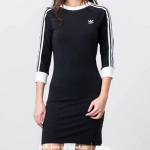 Svart klänning från Adidas - Säljer en cool svart klänning från Adidas med de klassiska tre ränderna i vitt längs ärmarna. Klänningen har en sportig stil med trekvartsärm och en bekväm passform. Perfekt för en avslappnad dag eller en sportig look!