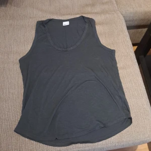 Mõrkgrå ärmlös linnetopp - Säljer en enkel och stilren svart ärmlös linnetopp. Perfekt för sommardagar eller som basplagg under en jacka. Toppen är i mjukt material och har en rund halsringning.