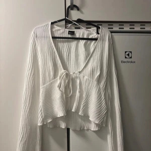 Vit ribbad blus från Gina Tricot - Säljer en superfin vit blus från Gina Tricot i storlek S. Den har en v-ringad design med knytning framtill och volangdetaljer. Perfekt för både vardag och fest! 💫köpte i somras för en fest, sedan dess är den orörd 
