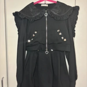 Svart klänning med spets och hjärtdetaljer Jirai Kei - Säljer en superfin svart set med spetsdetaljer och hjärtformade knappar. Den har en söt volangkrage och  framtill  hjärtformad dragkedja. Kragen kan bäras som en luva om ihop zippad eller som sailor krage! Kjolen är kort med spetskant. Perfekt för höst och vinter🖤Från det japanska märket Dear My Love, perfekt för casual jirai kei dagar 💕 både toppen och kjolen har fickor