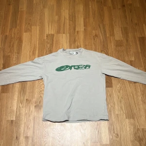 Beige långärmad tröja från Weekday - Säljer en beige långärmad tröja från Weekday i storlek XS. Tröjan har ett grönt tryck både fram och bak, vilket ger den en cool och avslappnad stil. Perfekt för vardagsbruk eller en chill dag ute. Materialet känns mjukt och bekvämt mot huden.