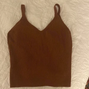 Brun ribbad linnetopp - Säljer en snygg brun ribbad linnetopp i mycket bra skick. Toppen har en v-ringad design och är perfekt för både vardag och fest. Den ärmlösa stilen gör den idealisk för varmare dagar eller som ett lager under en jacka.