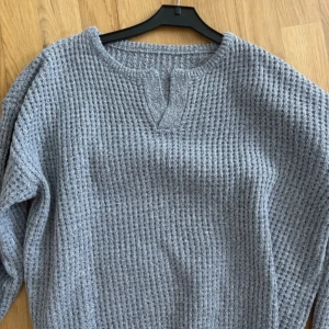 Grå stickad tröja - Mysig grå stickad tröja i ett snyggt, texturerat mönster. Perfekt för kyliga dagar med sin bekväma passform och långa ärmar. Den har en enkel men stilren design som funkar till det mesta. Ett måste i garderoben för höst och vinter!