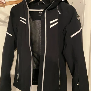 Svart jacka från Icepeak - Säljer en svart jacka från Icepeak i mycket bra skick. Den har en sportig look med vita detaljer och dragkedja. Perfekt för höst och vår. Jackan har en huva och långa ärmar, vilket gör den idealisk för kyligare dagar.