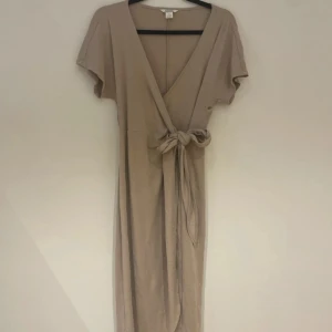 Beige omlottklänning från Monki - Säljer en superfin beige omlottklänning från Monki i storlek S. Klänningen har korta ärmar och ett knytband i midjan för en smickrande passform. Perfekt för både vardag och festliga tillfällen. Materialet är mjukt och bekvämt, vilket gör den idealisk för vår och sommar.