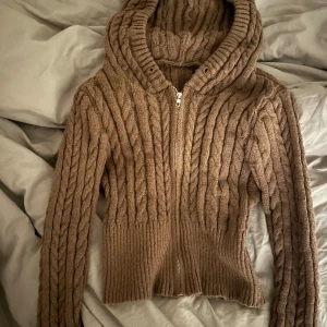 Brun stickad hoodie - Strl L men passar en S/M bättre!          Mysig brun stickad hoodie med dragkedja framtill. Perfekt för kyliga dagar med sin varma och bekväma design. Den har en ribbad struktur och en skön huva som håller dig varm. Passar perfekt till både vardag och avslappnade tillfällen.