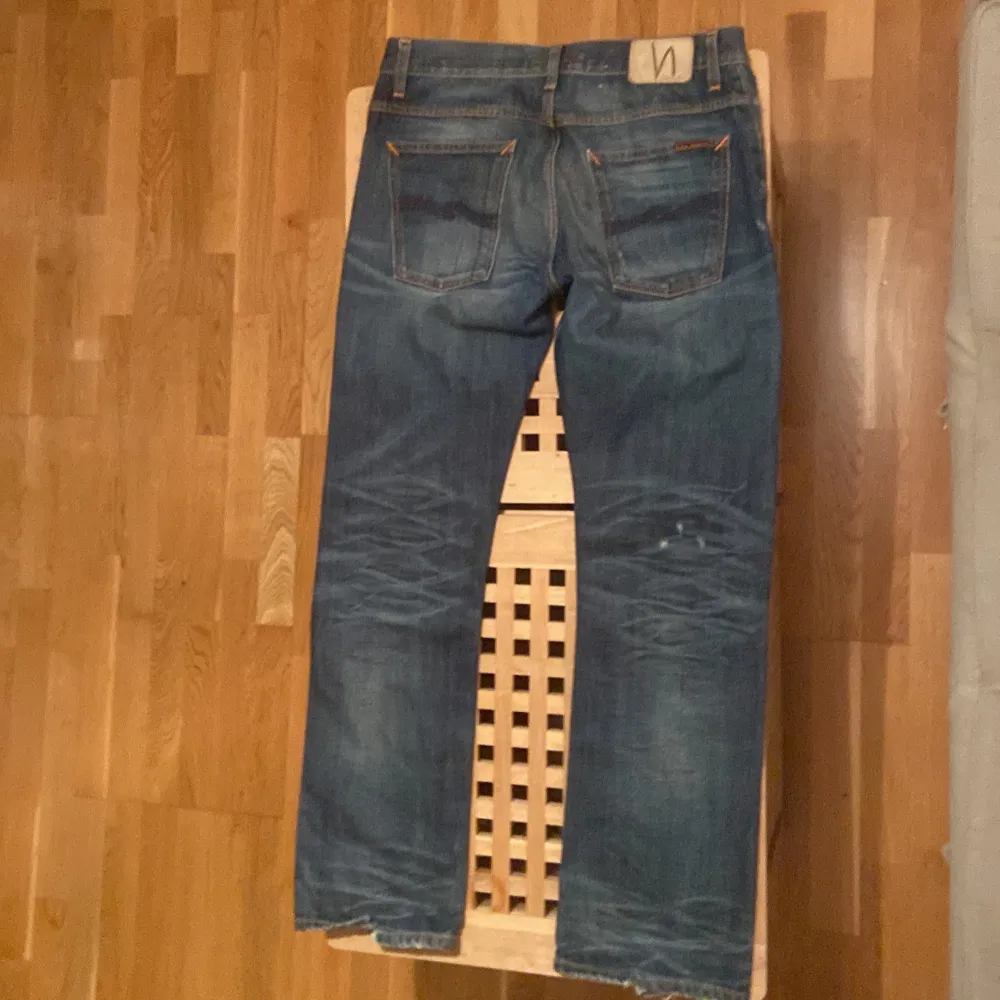 Säljer ett par snygga blå jeans med coola slitningar på framsidan. De har en klassisk femficksdesign och en knappgylf. Perfekta för en avslappnad stil och passar till de flesta tillfällen. Skicket är bra med en skön, inburen känsla.. Jeans & Byxor.