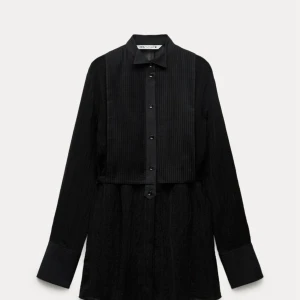 Svart långärmad skjorta från Zara - Snygg svart långärmad skjorta från zara med klassisk krage och knappar framtill. Skjortan har en elegant plisserad detalj på bröstet. Oanvänd. Strl 36.