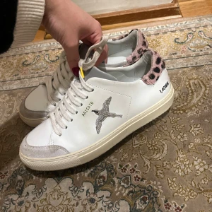  Axel Arigato clean 90 - Säljer ett par snygga vita sneakers från Axel Arigato. De har en cool fågelbrodering på sidan och leopardmönstrad detalj vid hälen. Skorna är i nästan nyskick då jag endast haft de i två månader vid vissa tillfällen. Påsen följer med