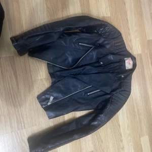 Svart skinnjacka med dragkedjor - Säljer en snygg svart skinnjacka i mycket bra skick. Den har coola dragkedjor och quiltade detaljer på axlarna. Perfekt för höst och vår, och funkar lika bra till fest som till vardags. Jackan har en tight passform och ger en edgy look. Jackan är i storlek 36. Köpt från Chiquelle.