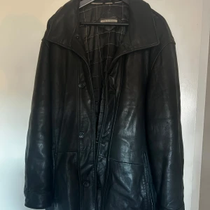 Vintage svart skinnjacka - Säljer en svart skinnrock i bra skick. Den har en klassisk design med knappar och en quiltad insida för extra värme. Perfekt för höst och vinter. Rocken har långa ärmar och en stilren look.