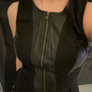 Svart korsett med dragkedja - Snygg svart korsett med dragkedja fram. Perfekt för en kväll ute eller en fest. Den har en tight passform och är gjord i ett skinnliknande material som ger en cool look. Passar bra till både byxor och kjol.