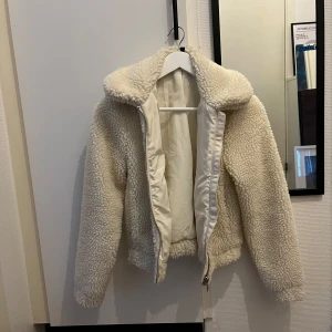 Vit teddyjacka - Supermysig vit teddyjacka som är perfekt för kyliga dagar. Den har en dragkedja framtill och en hög krage som håller dig varm. Jackan är i mycket bra skick och passar perfekt till både höst och vinter. Den är långärmad och har en normal passform. Perfekt för att hålla stilen och värmen samtidigt!