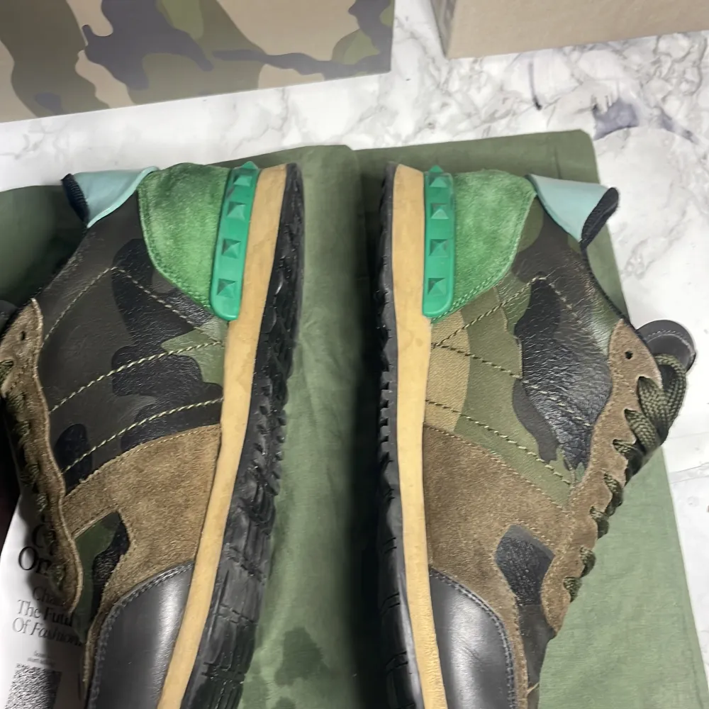 Säljer ett par Valentino Rockrunner sneakers de är i storlek 41men passar 42i camouflage. Skorna har en cool mix av grönt, brunt och svart med detaljer i mocka och skinn. De har en unik design med snörning och en grön häl med nitar. Perfekta för att sticka ut i mängden! . Skor.