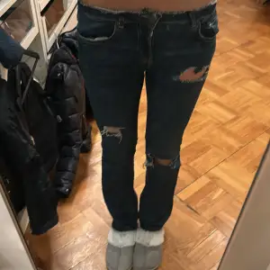 Säljer ett par mörkblå jeans i bra skick med coola slitningar på låren och knäna. De har en fin passform och är lågmidjade, vilket ger en snygg och modern look. Perfekta för en avslappnad vardagsstil eller en utekväll. Passar bra med både sneakers och klackar!