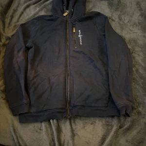 Mörkblå hoodie från Sail Racing - Säljer en mörkblå hoodie från Sail Racing i bra skick. Den har en dragkedja framtill och en broderad logga på bröstet och huvan. Perfekt för höst och vinter, och den är superbekväm att ha på sig. Passar både till vardags och lite mer avslappnade tillfällen.