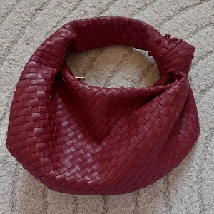 Vinröd flätad axelväska - Snygg vinröd axelväska i flätat skinnmaterial som är väldigt trendig just nu, passar perfekt till vardags eller finare outfits. Köpte den från bohoo för 500kr ungefär. Den är i nyskick köpt för någon månad sedan och använd någon enstaka gång❤️ 