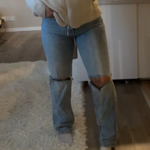 Jeans från Gina Tricot storlek 38 - Säljer ett par snygga blå jeans med slitningar på knäna, perfekta för en trendig look. Köpta på Gina Tricot, storlek 38.  Skick: Använda endast ett fåtal gånger och i mycket fint skick.