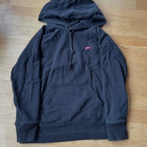 Svart hoodie från Levi's - Säljer en svart hoodie från Levi's i bra skick. Den har en klassisk design med en känguruficka och justerbar huva. Använd ett par gånger men fortfarande i bra skick. 100 % bomull 🤍