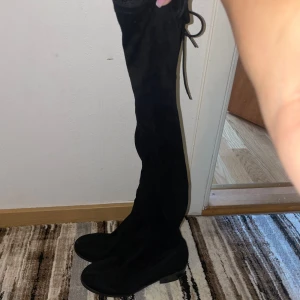 Svarta overknee stövlar - Säljer ett par snygga svarta overknee stövlar i mocka. De har en låg klack och snörning baktill för en justerbar passform. Perfekta för höst och vinter, både stiliga och bekväma. Passar till både vardag och fest!