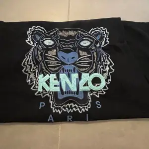 Säljer en svart t-shirt från Kenzo med ett coolt tigertryck i blått och grönt på framsidan. T-shirten är kortärmad och har en normal passform. Perfekt för en avslappnad stil eller att bära till fest. 🐯