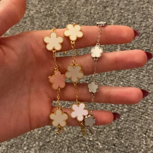 Blomformade armband i guld och silver - Säljer tre superfina armband med blomformade hängen. Ett armband är i guld med vita blommor, ett annat i guld med rosa och vita blommor, och det tredje i silver med vita blommor. Perfekta för att ge en söt touch till din outfit (säljer alla för 11kr tillsammans). 