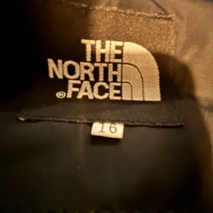 Svart pufferjacka från The North Face - Säljer en svart pufferjacka från The North Face i storlek 16. Jackan har en quiltad design med dragkedja och två praktiska fickor. Insidan har ett coolt mönster som ger extra stilpoäng. Perfekt för höst och vinter!