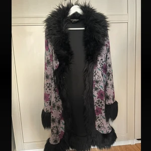 Blommig kappa med fuskpäls från Velvet Kitten - Säljer en unik och snygg kappa från Velvet Kitten i storlek S. Den har ett blommigt mönster i lila och rosa med svart fuskpäls längs kanterna och ärmsluten. Riktigt häftig lägg realistiska prisförslag 🔥