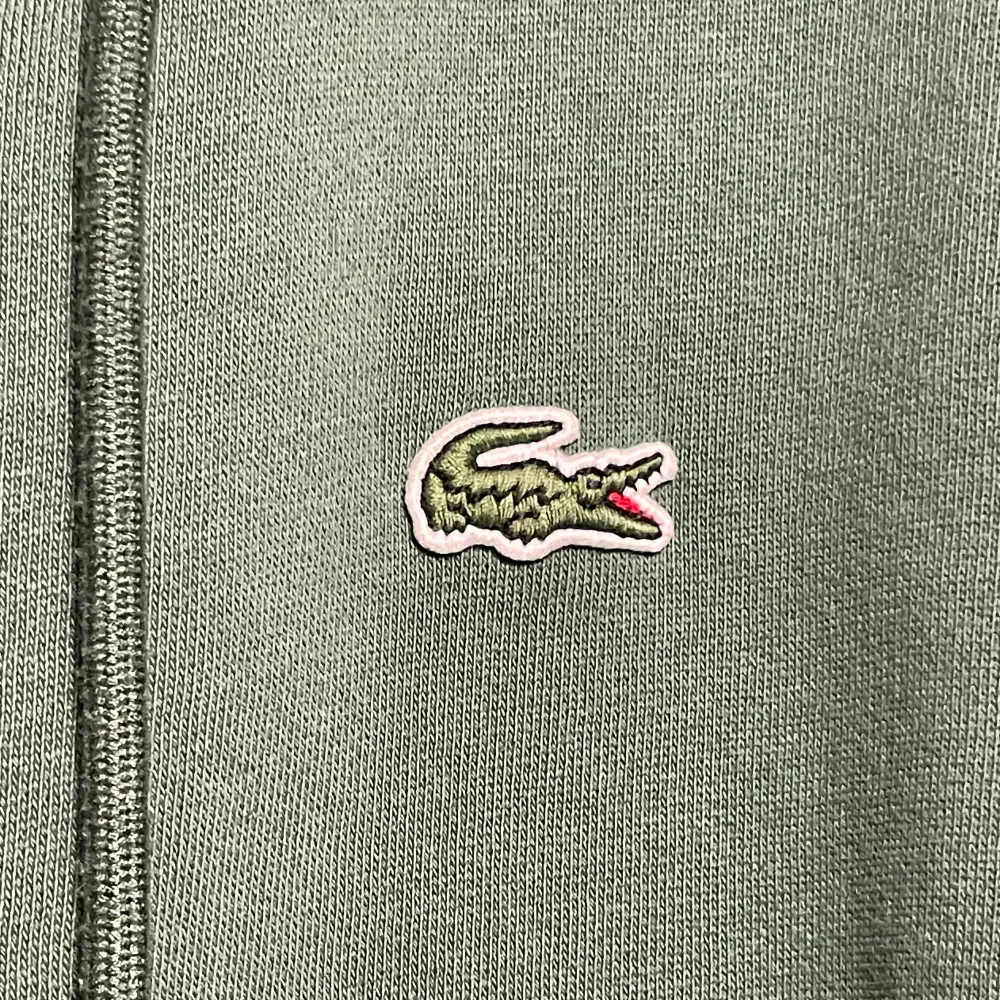 Säljer en snygg grön hoodie från Lacoste i storlek M. Den har en dragkedja framtill och den klassiska krokodilloggan på bröstet. Perfekt för både höst, vinter och vår, med en skön passform och huva för extra mysfaktor. Passar lika bra till vardags som till träning! Tröjan är dock lite mindre än sin storlek. Säljer tröjan eftersom den var för liten. Tröjan har även använts endast ett fåtal gånger men köptes för drygt ett år sedan. Nypris: 1600. Priset är inte hugget i sten!. Hoodies.