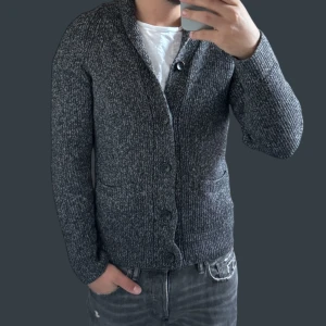 Grå stickad kofta - Säljer en snygg grå stickad kofta med knappar framtill. Perfekt för kyliga dagar och passar både till vardags och lite finare tillfällen. Koftan har långa ärmar och två praktiska fickor. Den är i bra skick och superbekväm att ha på sig. Perfekt för höst och vinter!