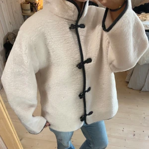 Vit teddyjacka med svarta detaljer - Superfin vit teddyjacka med svarta knappar och kantdetaljer. Perfekt för höst och vinter! Den är långärmad och har en mysig, loose passform. Jackan är i mycket bra skick och passar perfekt för kyliga dagar. 🖤VÄLDIGT eftertraktad och helt slutsåld💕💕