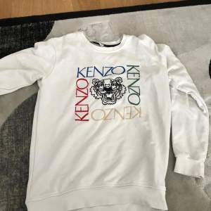 Säljer en snygg vit sweatshirt från Kenzo med färgglatt tryck och ikonisk tiger. Tröjan har långa ärmar och är perfekt för en casual look. Passar både till vardags och festliga tillfällen. Superbekväm och stilren!