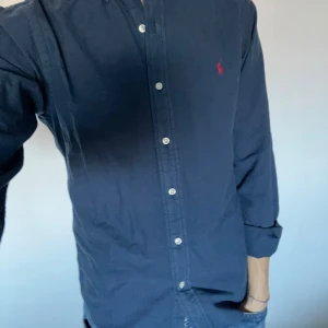 Ralph Lauren skjorta - Säljer en snygg mörkblå skjorta från Ralph Lauren i slim. Den är perfekt för både vardag och fest. Den klassiska designen med den lilla röda loggan på bröstet ger en stilren look. Passar perfekt till jeans. Hör gärna av er vid funderingar eller frågor!